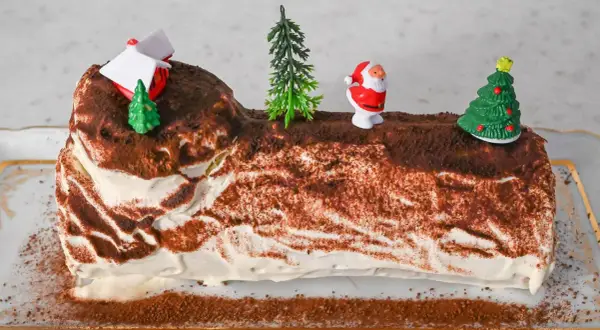 Eine festliche Bûche de Noël, dekoriert mit Weihnachtsmann, Bäumen und einem Haus.