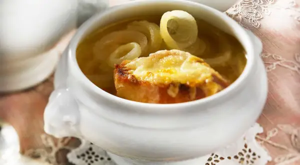 Herzhaftes Zwiebelsuppe Rezept Original: goldbraun überbackenes Brot mit geschmolzenem Käse auf Zwiebelringen in Brühe.
