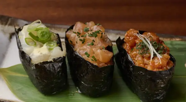 Drei leckere Sushi Gunkan mit Lachs, Garnelen und Fisch, garniert mit Frühlingszwiebeln und Kräutern.