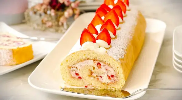 Ein köstlicher Brazo de Reina, gefüllt mit Sahne und Erdbeeren, dekoriert mit frischen Erdbeeren und Puderzucker.