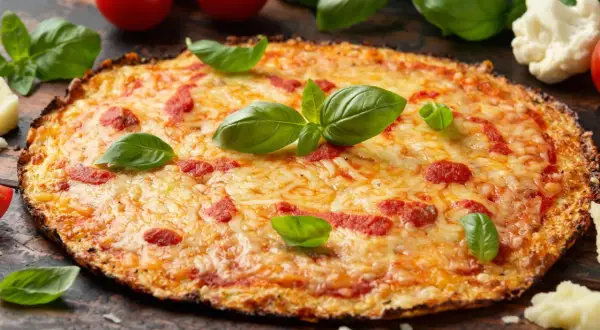 Eine köstliche blumenkohl pizza vegan, belegt mit Tomaten und Käse, garniert mit frischem Basilikum.