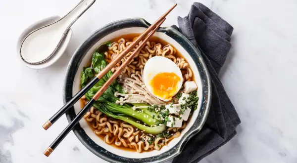 Schüssel mit japanischem Ramen, Nudeln, Ei, Gemüse und Tofuwürfeln, garniert mit Sesam und Schnittlauch.