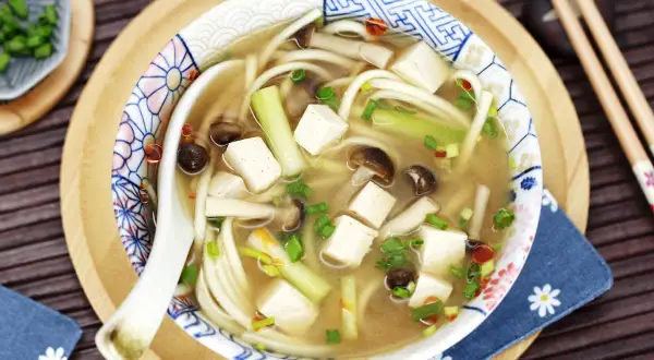 Herzhafte Miso Udon Suppe mit Tofu, Pilzen und Frühlingszwiebeln, serviert in einer dekorativen Schale.