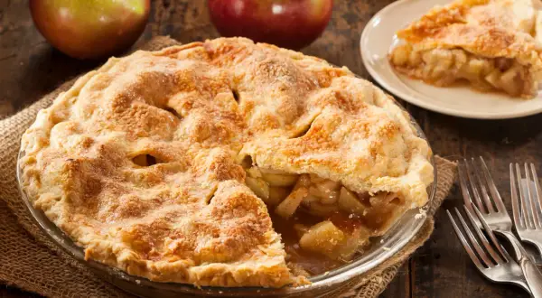 Goldbrauner Apfelkuchen, ein Klassiker der american pie recipe, mit saftiger Füllung und knusprigem Teig. Daneben Äpfel und Gabeln.
