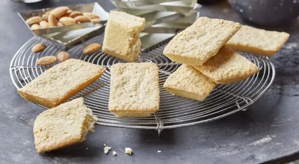 Goldbraune Financiers, frisch aus dem Ofen, warten auf das Financier Rezept. Mandeln liegen daneben.