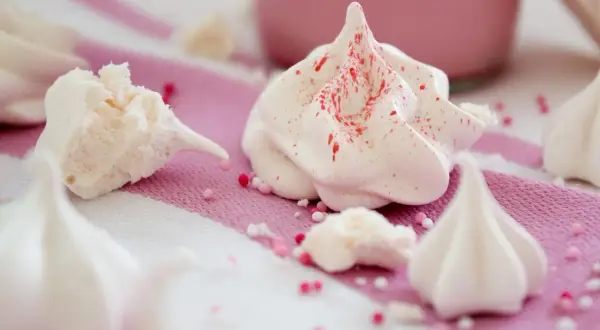 Zarte Baisers, frisch aus dem Ofen, sind nach dem Backen leicht klebrig. Kleine Zuckerperlen zieren die süßen Leckereien.