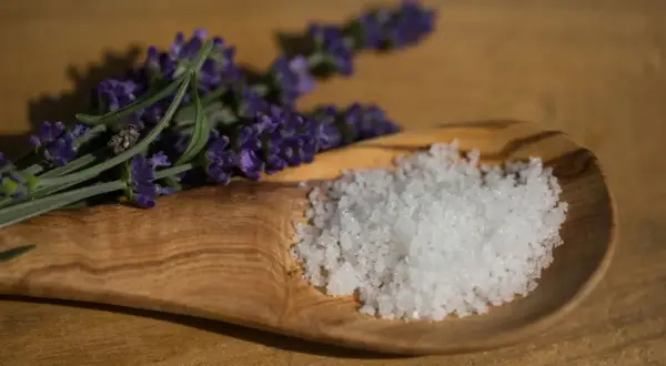 Fleur de Sel, feine Meersalzkristalle, auf einem Olivenholz-Löffel neben Lavendel. Was ist Fleur de Sel? Ein Hauch von Luxus für Ihre Küche.