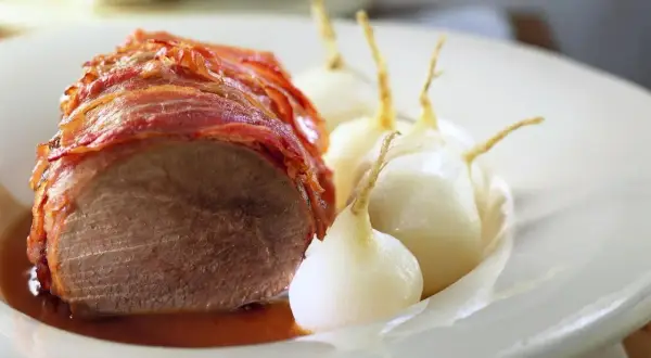 Boeuf à la mode: Ein saftiges Stück Rindfleisch, umwickelt mit knusprigem Speck, serviert mit kleinen, glasierten Zwiebeln in einer köstlichen Sauce.