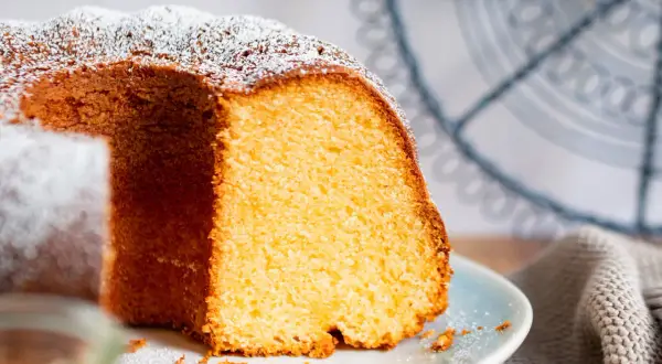 Saftiger Kuchen mit 12 Eiern, bestäubt mit Puderzucker, auf einem Teller mit einem Stück herausgeschnitten.