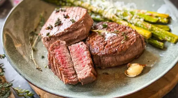Zartes Filet de Boeuf, perfekt medium-rare gebraten, serviert mit grünem Spargel und einer Knoblauchzehe. Ein Festmahl!