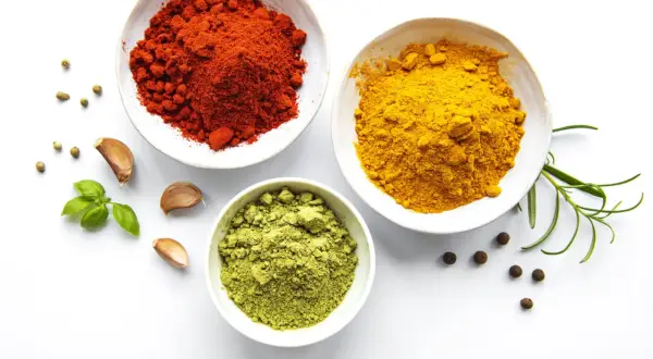 Schalen mit roten, gelben und grünen Gewürzen, Knoblauch und Kräutern – die Zutaten, woher kommt Curry.