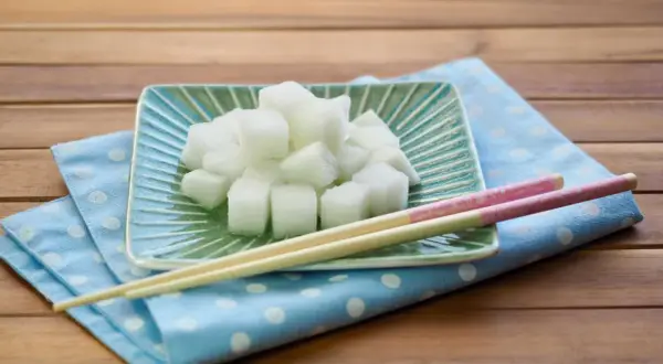 Würfel von daikon rettich auf einem grünen Teller, daneben Stäbchen auf einem blauen Tupftuch.
