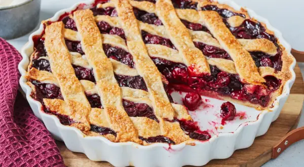 Ein frisch gebackener Kirschkuchen mit Gittermuster, perfekt für ein Kirschkuchen Rezept. Daneben eine Schüssel Schlagsahne.