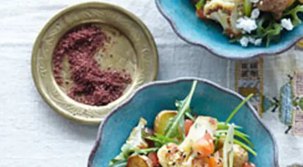Gewürzschale mit rotem Pulver, vielleicht eine Sumach-Alternative, neben einem bunten Salat mit Blumenkohl und Ziegenkäse.