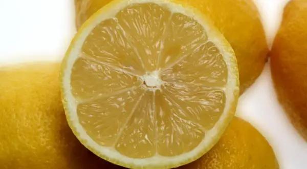 Ein aufgeschnittenes, saftiges Zitronenstück liegt auf ganzen Zitronen. Die Zitronenschale ist gesund und voller Vitamine.