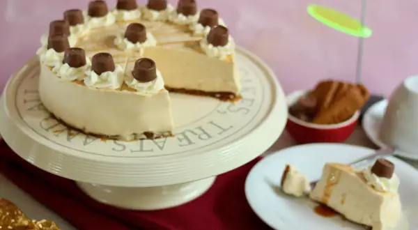 Eine köstliche karamell torte, verziert mit Sahnetuffs und Schokoladenstückchen, steht auf einem Tortenständer. Ein Stück ist bereits auf einem Teller angerichtet.