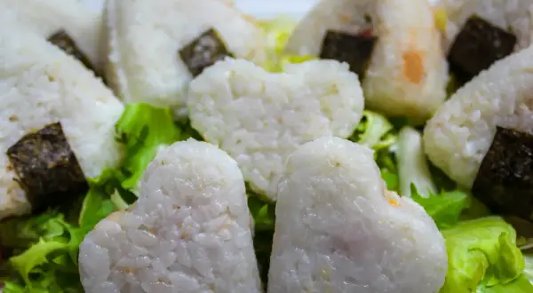 Herzförmige und dreieckige japanische Gerichte mit Reis, umhüllt von Nori-Algen, serviert auf knackigem Salat.
