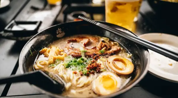 Herzhaftes Shoyu Ramen mit zartem Schweinefleisch, perfekt gekochtem Ei und Frühlingszwiebeln. Daneben ein kühles Bier.