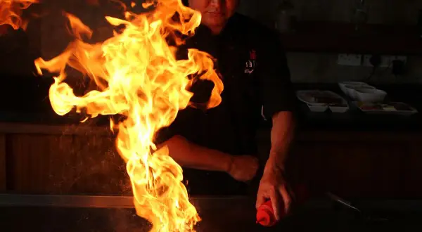 Ein Koch inszeniert mit flammendem Spektakel, was ist Teppanyaki: eine Showküche mit Feuer und Sauce.