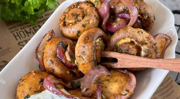 Gefüllte champignons aus dem airfryer mit roten Zwiebeln und Kräutern, serviert mit Dip.