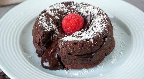 Schokokuchen mit weichem Kern, bestäubt mit Puderzucker und garniert mit einer Himbeere. Der flüssige Kern läuft verführerisch heraus.