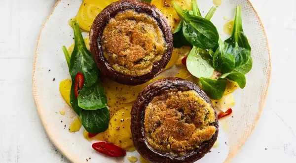 Zwei gefüllte Portobello Pilze auf gelben Ringen, garniert mit frischem Grün und Chilischeiben.