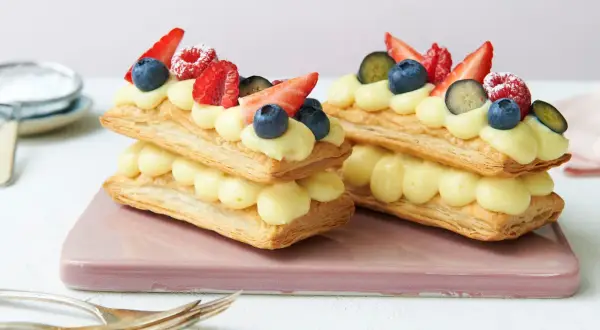 Zwei Mille-feuille-Törtchen mit Vanillecreme und frischen Beeren, bereit zum Genießen.