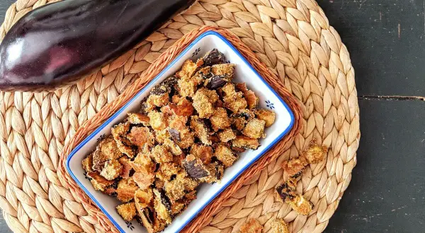 Knusprige, frittierte Aubergine in einer Schale, daneben eine ganze Aubergine. Ein leckerer Snack!