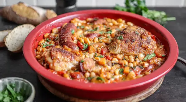 Herzhaftes Cassoulet Rezept in roter Auflaufform mit Hähnchen, Wurst und weißen Bohnen, garniert mit Petersilie.