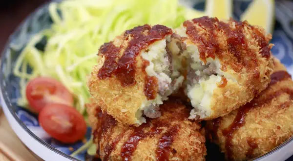 Knusprige japanische Kroketten, gefüllt mit Kartoffelpüree und Hackfleisch, serviert mit Salat und Tomaten.