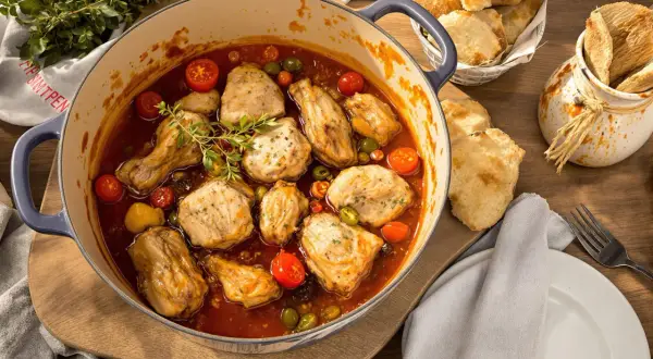 Herzhaftes Poulet Basquaise in einem Topf, mit Tomaten, Oliven und Kräutern, serviert mit Brot.