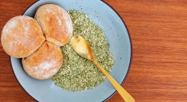 Drei Brötchen liegen auf einem Teller neben einer grünen Mischung, die zeigt, was ist schabzigerklee. Eine goldene Löffel liegt darin.