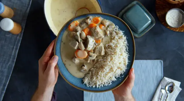Ein Teller mit cremigem Blanquette de veau, Pilzen und Karotten, serviert mit Reis.