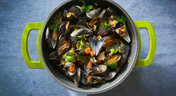 Ein Topf voller dampfender Moules Marinière, garniert mit frischer Petersilie und Karottenstücken, bereit zum Genuss.