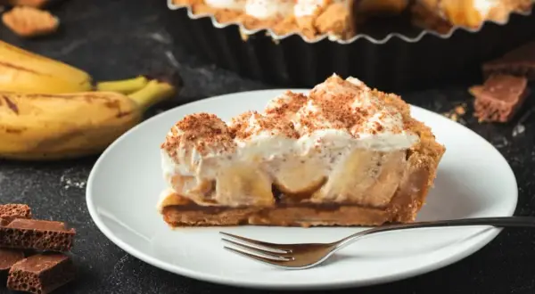 Ein Stück Banoffee Pie mit Bananen, Karamell und Sahne, bestreut mit Kakaopulver. Perfekt für Ihr Banoffee Pie Rezept!