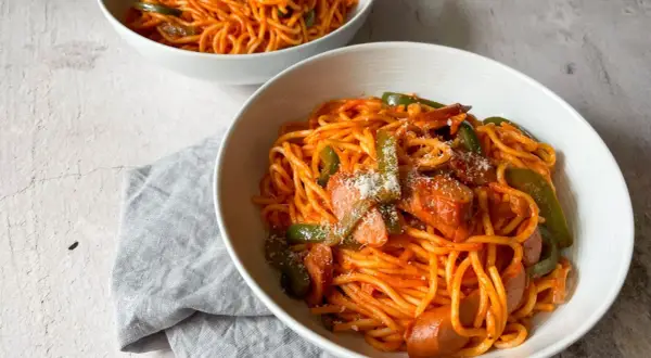 Zwei Schüsseln mit leckerem Spaghetti Napolitan, garniert mit Paprika und Wurst.
