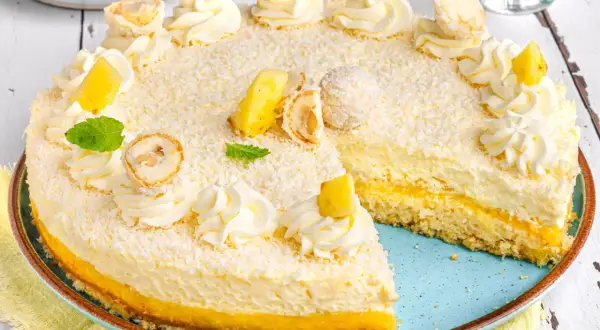 Ein köstlicher Ananas Kokos Kuchen, verziert mit Kokosraspeln, Sahnetuffs, Ananasstücken und Minze.