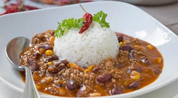 Herzhaftes Chili con Carne mit Reis, garniert mit Petersilie und einer getrockneten Chili.