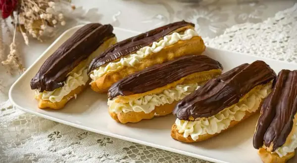 Fünf köstliche Éclairs mit Schokoladenglasur und Sahnefüllung auf einer weißen Platte, perfekt für ein Éclair-Rezept.