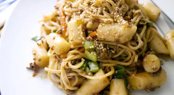 Yaki soba mit Hackfleisch, Möhren, Frühlingszwiebeln und Tteok (Reiskuchen), bestreut mit Sesam.