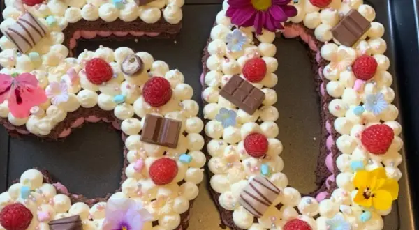 Ein aufwendig dekorierter Number Cake in Form der Zahl 50, verziert mit Sahnetuffs, Himbeeren, Schokolade und Blumen.