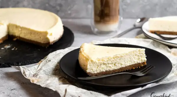 Ein Stück cremiger American Cheesecake, perfekt für das original american cheesecake rezept. Dazu ein Latte Macchiato.
