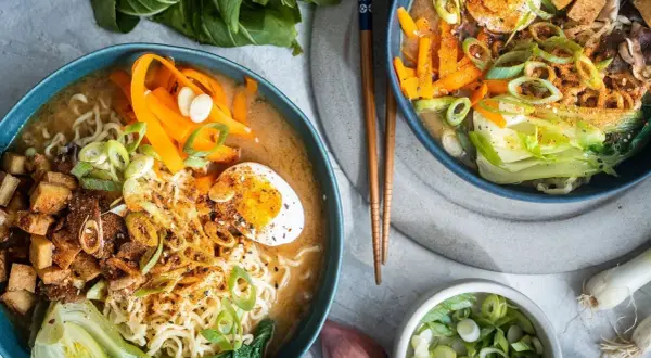 Zwei Schalen mit dampfendem, **vegetarischem Ramen**. Nudeln, Karottenstreifen, Pak Choi, Tofuwürfel und ein halbes Ei in herzhafter Brühe.