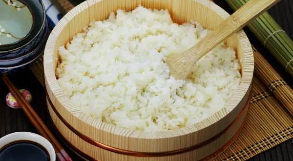Perfekt zubereiteter sushi reis in einem hölzernen Behälter, bereit für die Zubereitung von Sushi. Daneben liegen Stäbchen und Sojasauce.