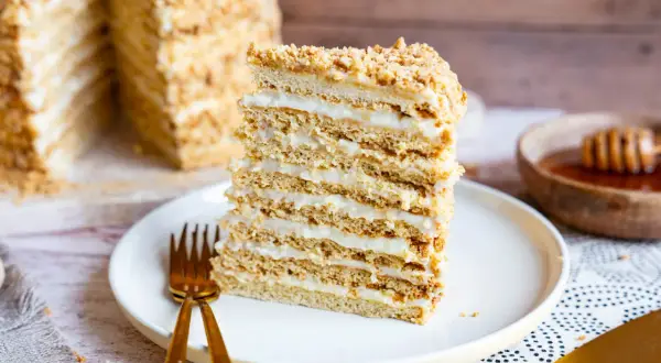 Ein Stück russischer Kuchen, geschichtet mit Honig und Sahne, auf einem Teller mit goldenem Besteck.
