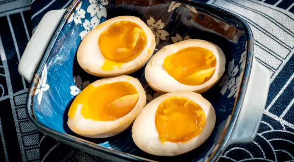 Vier halbe, perfekt gekochte ramen eier mit flüssigem Eigelb in einer blauen Schale mit Kirschblütenmuster.