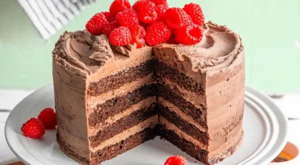 Saftige Mokkatorte mit Buttercreme, dekoriert mit frischen Himbeeren. Ein Stück ist herausgeschnitten, um die vielen Schichten zu zeigen.