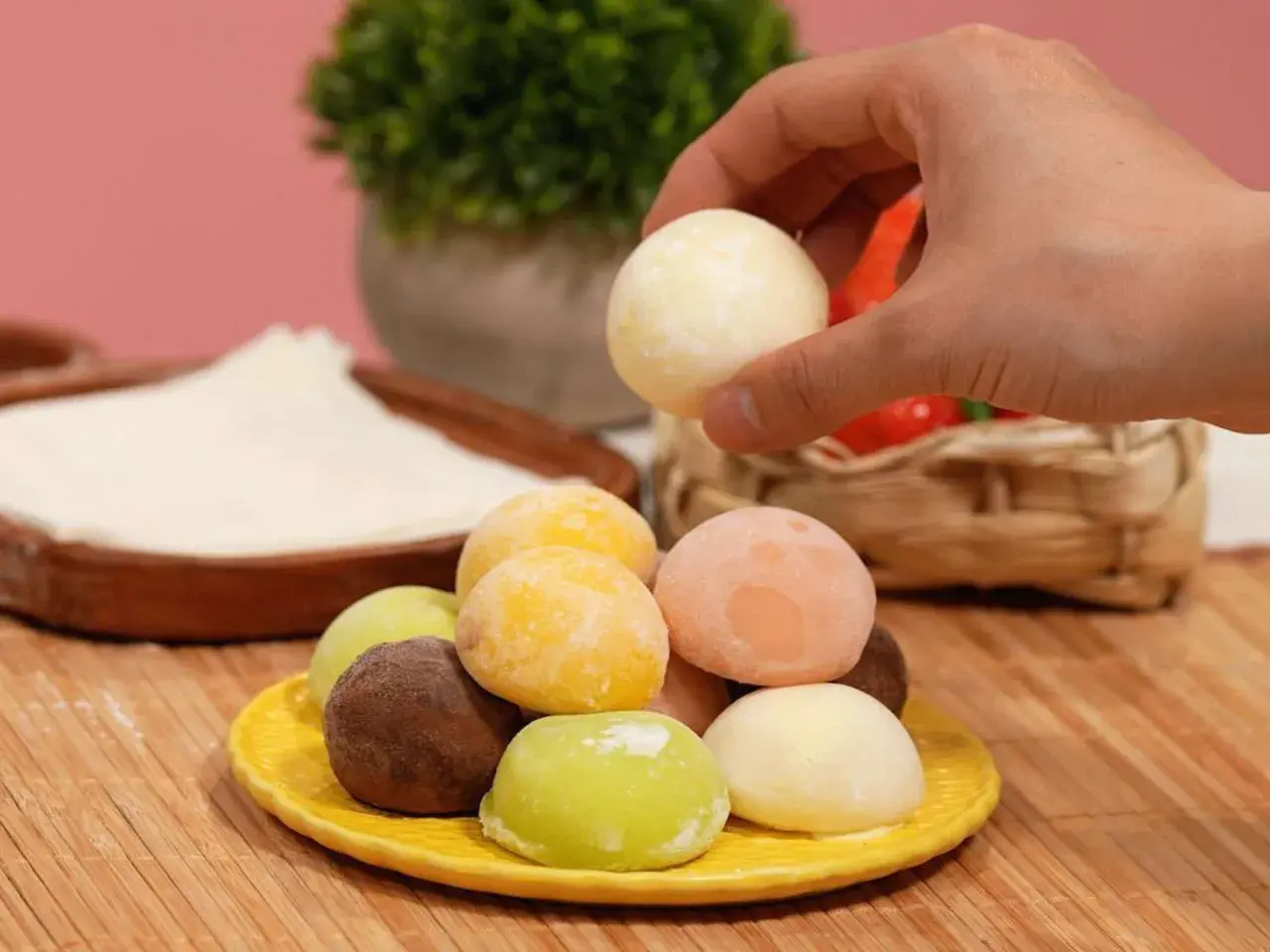 Bunte mochis eis in verschiedenen Geschmacksrichtungen auf einem gelben Teller. Eine Hand greift nach einem weißen mochi eis.
