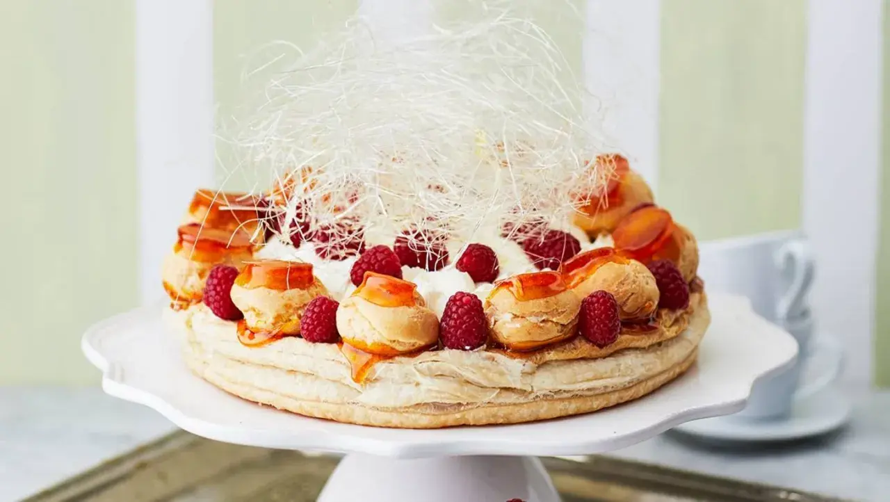 Ein prachtvoller Saint Honoré Kuchen mit Brandmasse-Profiteroles, frischen Himbeeren, Sahne und Karamellfäden.
