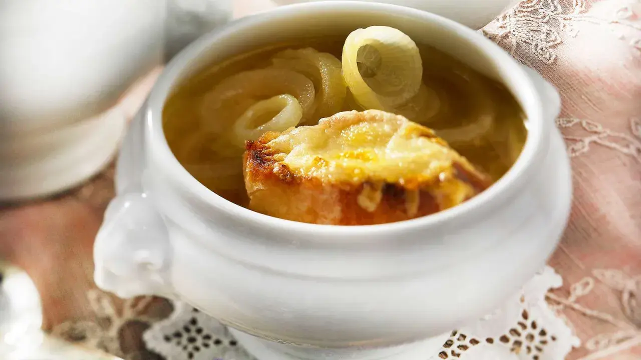 Herzhaftes Zwiebelsuppe Rezept Original: goldbraun überbackenes Brot mit geschmolzenem Käse auf Zwiebelringen in Brühe.